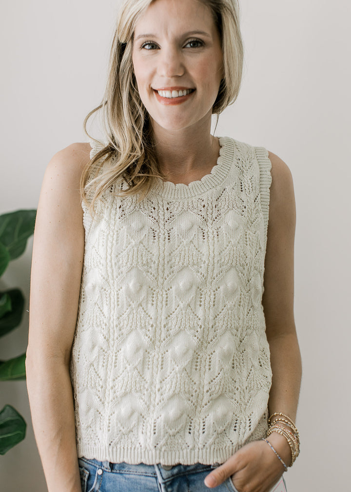 Model wearing a reversible cream knit sweater with brown buttons and scalloped detail. 