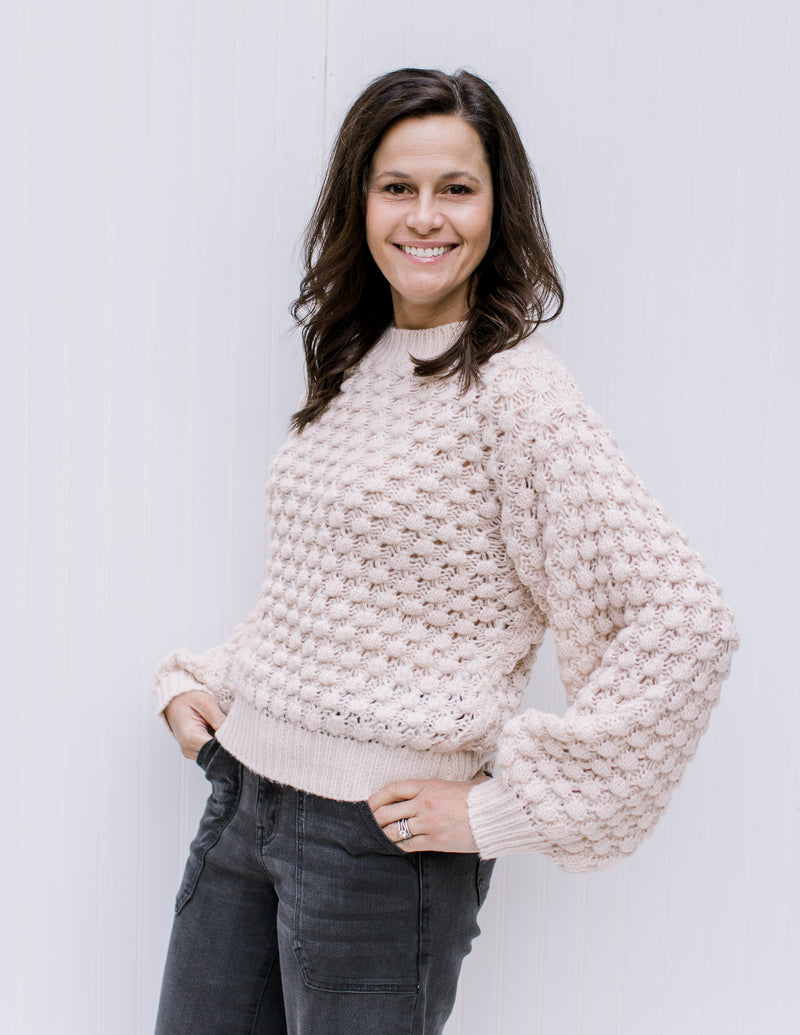 Model wearing a cream bubble knit sweater with bubble long sleeves and a round neckline. 