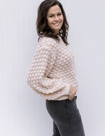 Model wearing jeans and a cream bubble knit sweater with bubble long sleeves and a round neckline. 