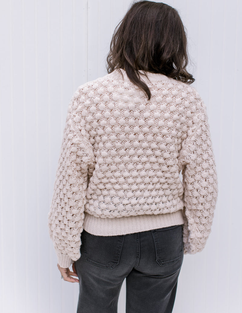 Back view of Model wearing a cream bubble knit sweater with bubble long sleeves and a round neck.