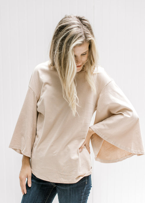 Model wearing a cream cotton top with a round neck and 3/4 butterfly sleeves. 