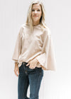 Model wearing jeans with a cream cotton top with a round neck and 3/4 butterfly sleeves. 