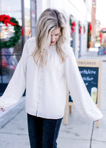 Model wearing a cream blouse with long sleeves with micro pleat detailing and a button front.