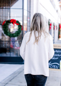 Back view of Model wearing a cream blouse with long sleeves and a button front.