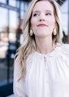 Close up of ruffle detail and buttons on a cream blouse with long sleeves and a round neck. 