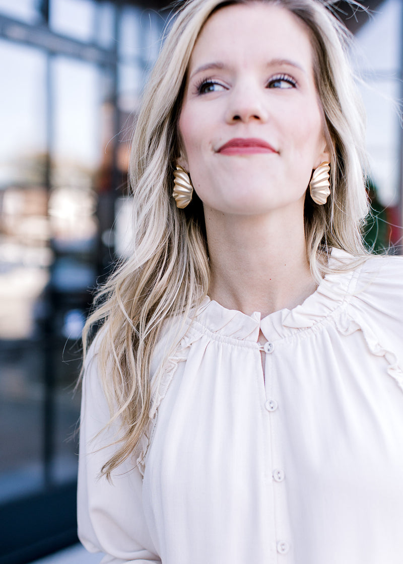 Close up of ruffle detail and buttons on a cream blouse with long sleeves and a round neck. 