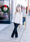 Model wearing jeans, booties and a cream blouse with long sleeves and a button front.