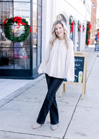 Model wearing jeans, booties and a cream blouse with long sleeves and a button front.