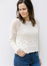 Model wearing a slightly cropped cream crochet sweater with long sleeves and scalloped hem.