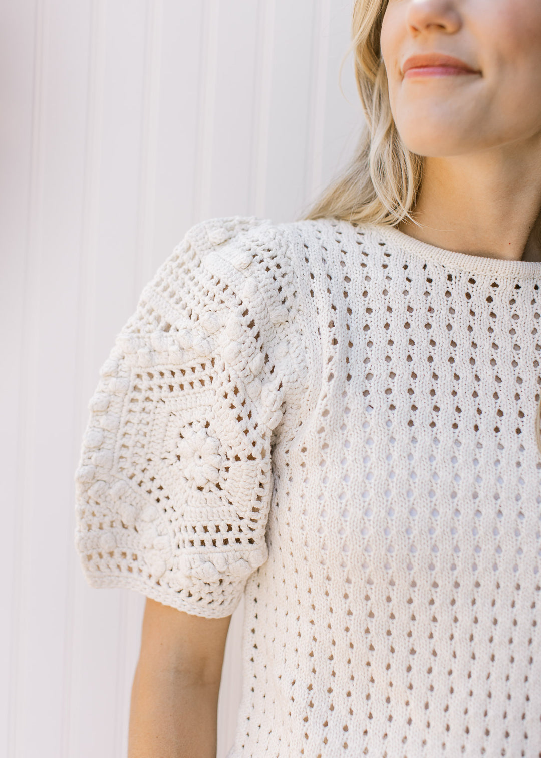 Close up of crochet detail on short puff sleeve of a cream sweater. 