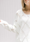Close up of diamond open stitch detail on a cream acrylic sweater with long sleeves and round neck.