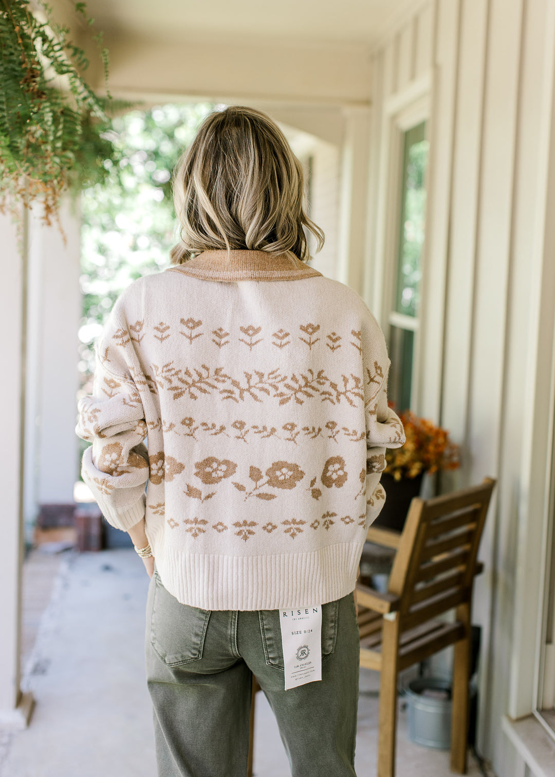 Back view of Model wearing a cream sweater with tan flowers, long sleeves and a tan flap collar.