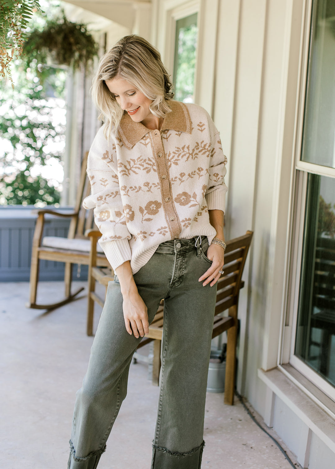Model wearing olive pants and a cream sweater with tan flowers, buttons and long sleeves.