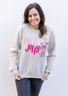 Model wearing a cream sweatshirt with a nutcracker and holly jolly in pink and long sleeves. 