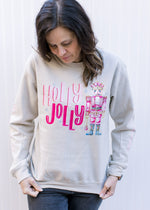 Close up of nutcracker and Holly jolly in pink on a cream long sleeve sweatshirt with crew neck.