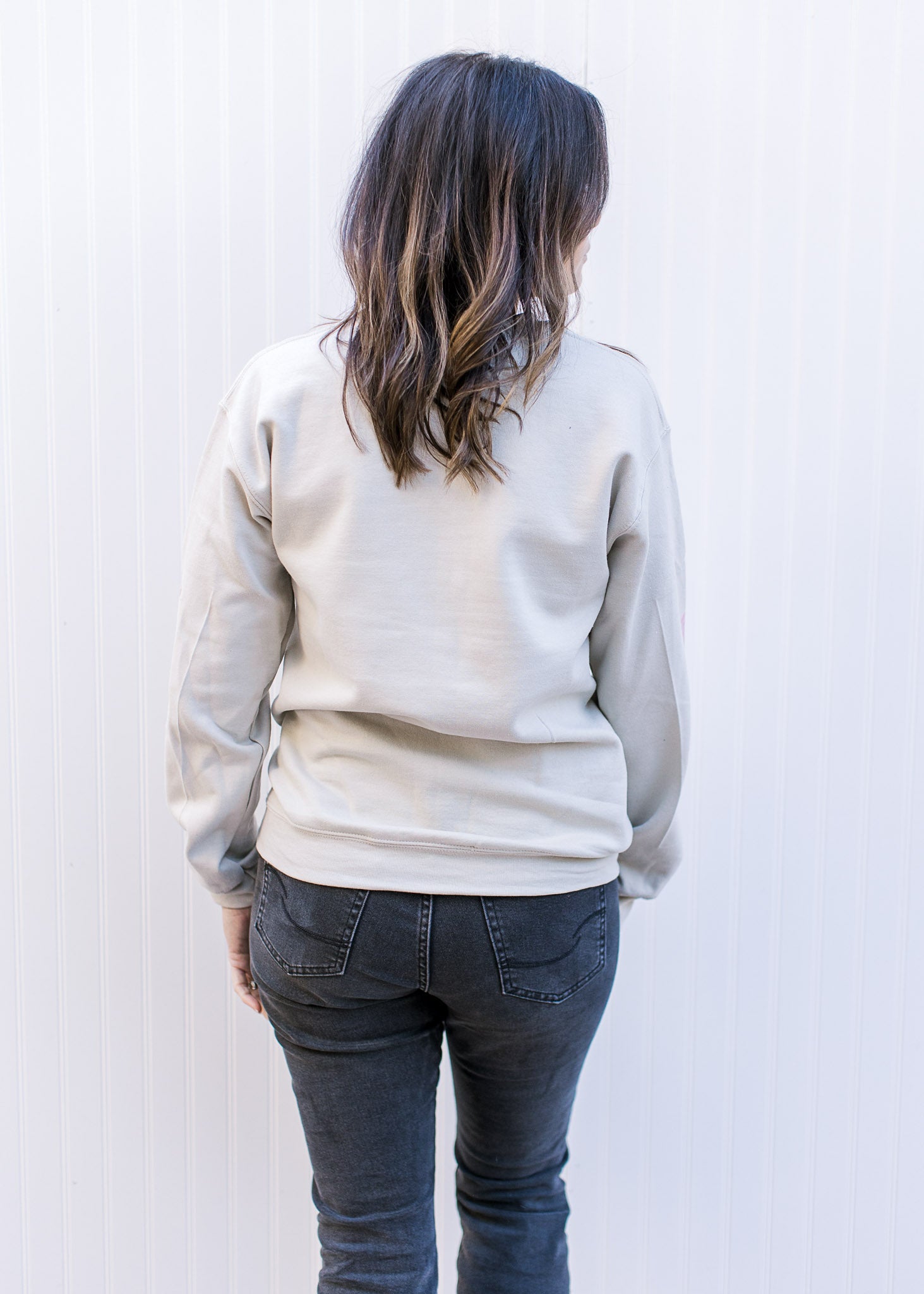 Back view of Model wearing a cream long sleeve sweatshirt with a nutcracker and holly jolly in pink
