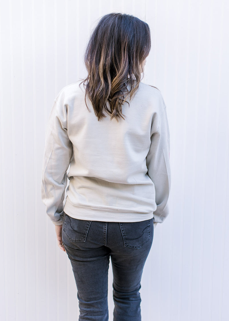 Back view of Model wearing a cream long sleeve sweatshirt with a nutcracker and holly jolly in pink