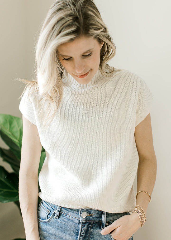 Model wearing a creamy knit top with a ribbed mock neck and hem and short drop sleeves. 