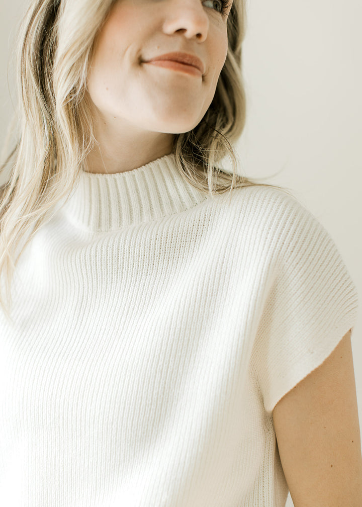 Close up of ribbed mock neckline and short drop sleeves on a lightweight cream sweater. 