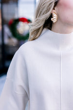 Close up of ribbed mock neck and extended shoulder on a cream oversized sweater. 