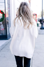 Back view of Model wearing a cream long sleeve sweater with a mock neck and extended shoulder. 