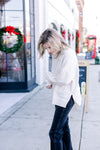 Side view of Model wearing a cream sweater with a mock neck, long sleeves and split sides.