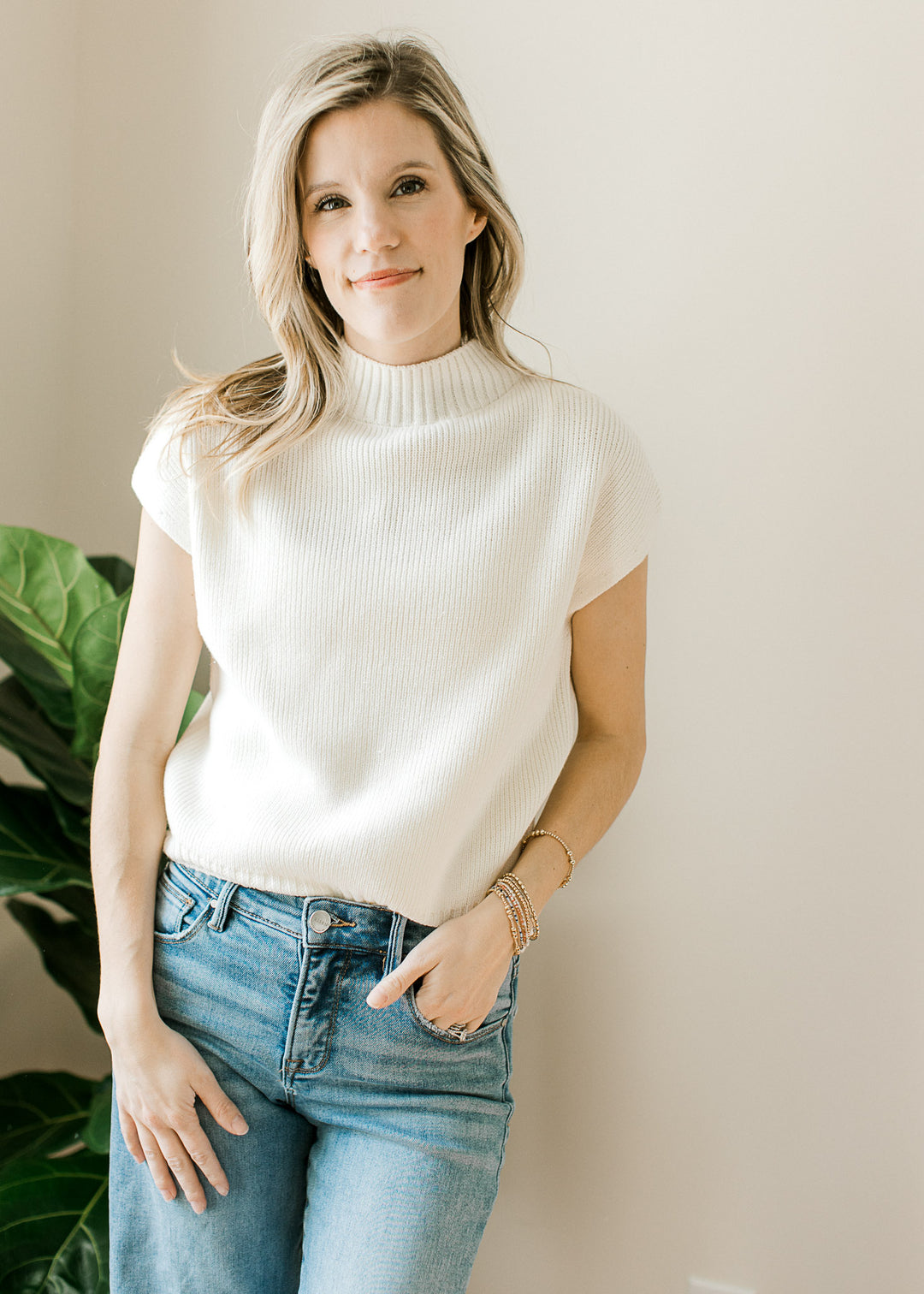 Model wearing jeans and a creamy knit top with a ribbed mock neck and hem and short drop sleeves. 