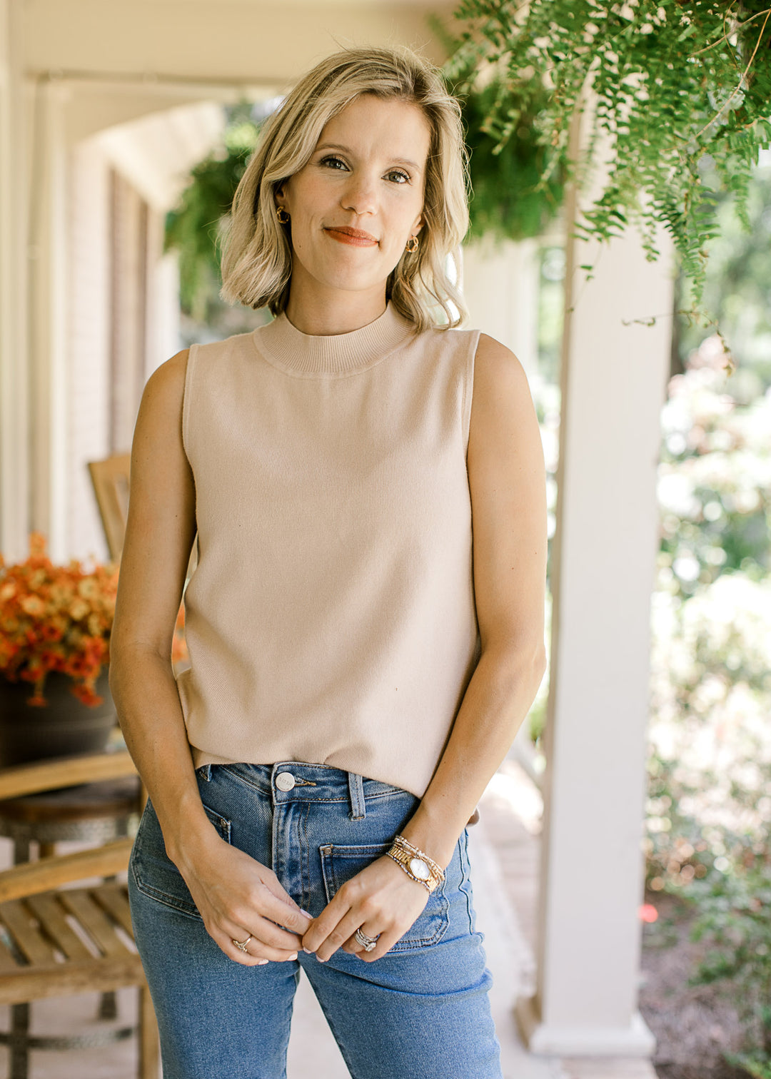Model wearing a cream sleeveless top with mock neck and ribbed material. 