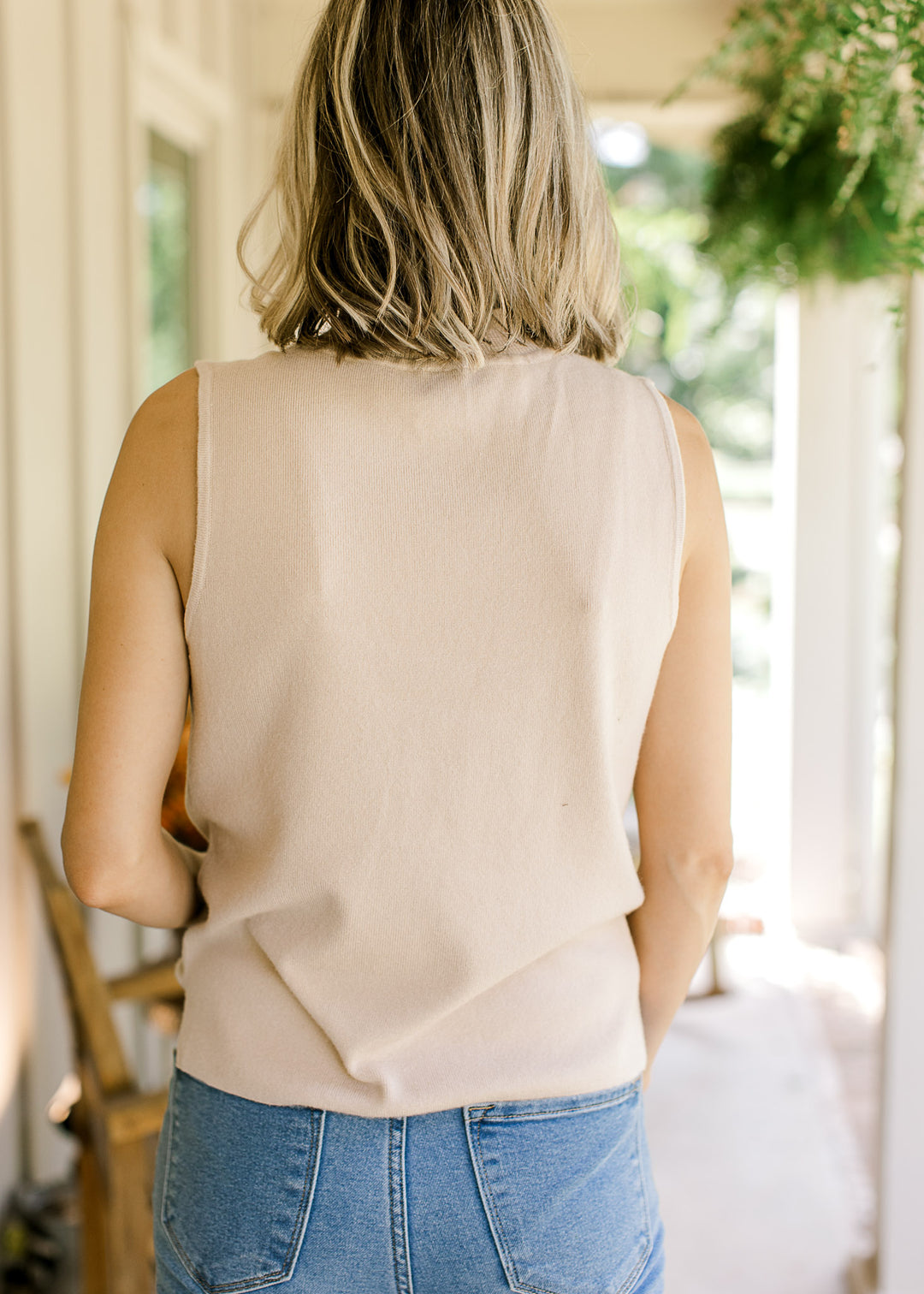Back view of Model wearing a cream sleeveless top with mock neck and ribbed material. 