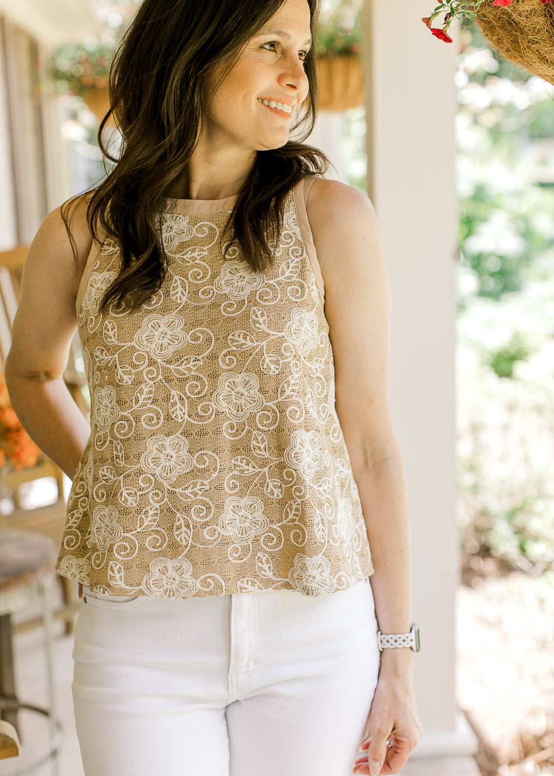 Model wearing a sleeveless camel top with cream floral stitching, round neck, keyhole back closure. 