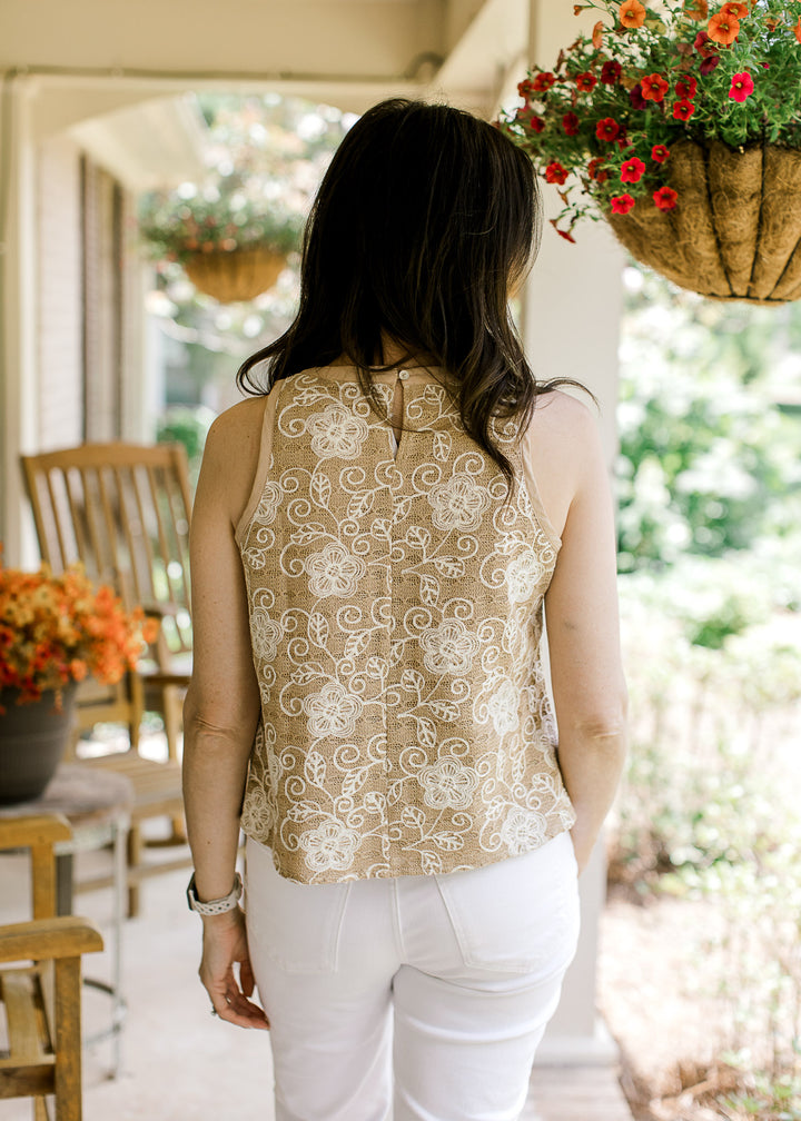 Back view of Model wearing a sleeveless camel top with cream floral stitching, and keyhole closure. 