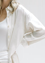 Close up view of sleeve and buttons on a cream oversized button up top made with a linen blend. 