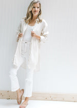 Model wearing a cream oversized button up top with white pants, a white bodysuit and sandals. 