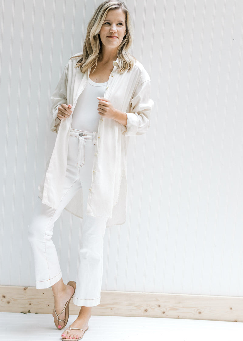 Model wearing a cream oversized button up top with white pants, a white bodysuit and sandals. 