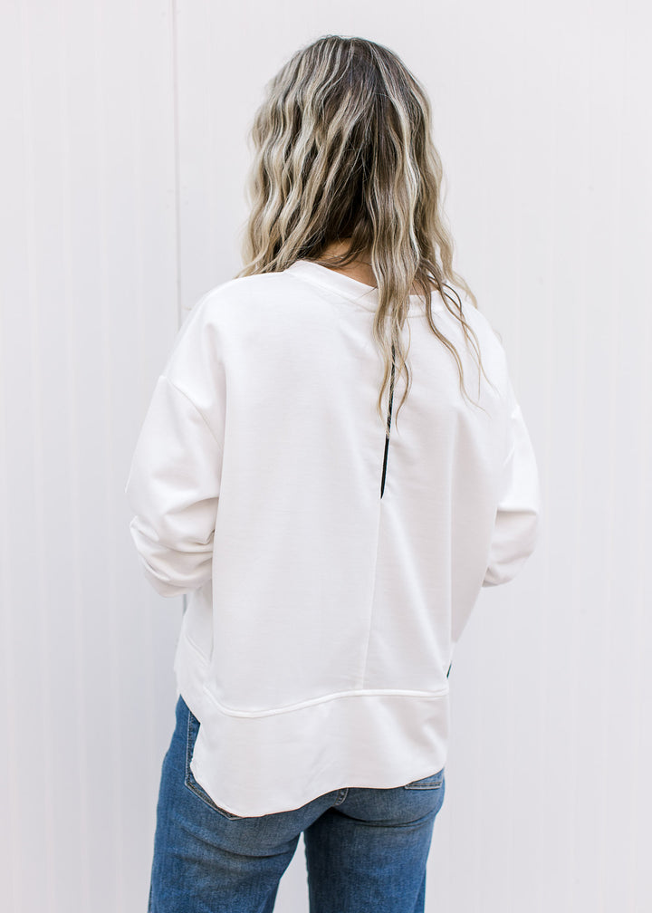 Back view of Model wearing a cream long sleeve top with black piping and patch pockets. 
