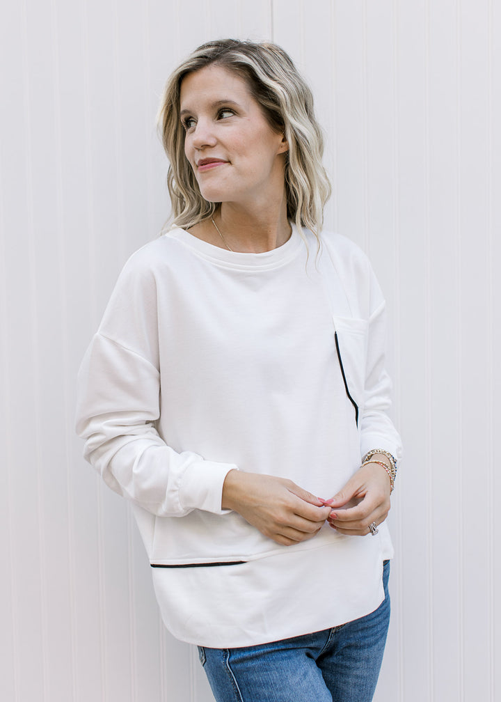 Model wearing a cream long sleeve top with black piping, patch pockets and a round neck. 