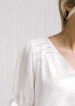 Close up of pleat detail on a model in a cream v-neck top with short sleeves. 