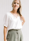 Model wearing a sage skirt with a cream v-neck top with a pleated shoulder detail and short sleeve. 
