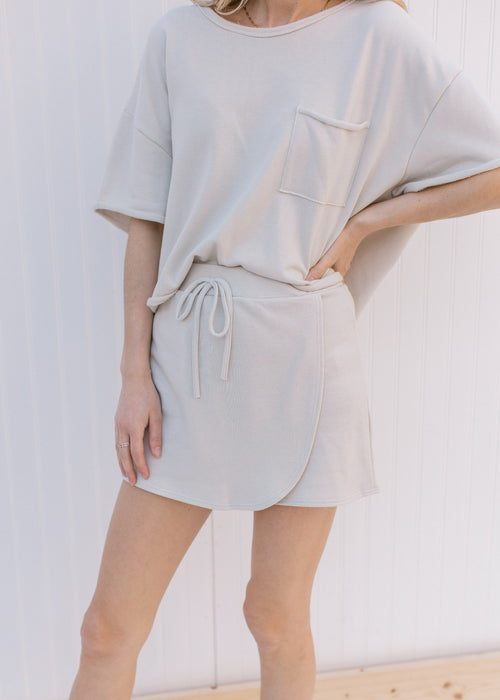 Model wearing a cream above the knee skort with a tie and cross over front panel.