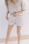 Model wearing a cream skort, holding up cross over front panel and exposing the shorts.