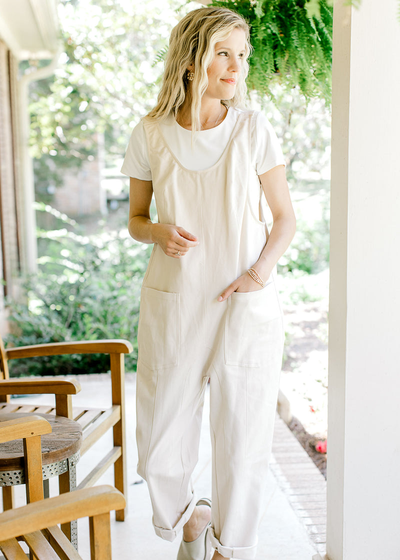 Model wearing a white top with cream denim jumpsuit with wide legs and adjustable straps. 