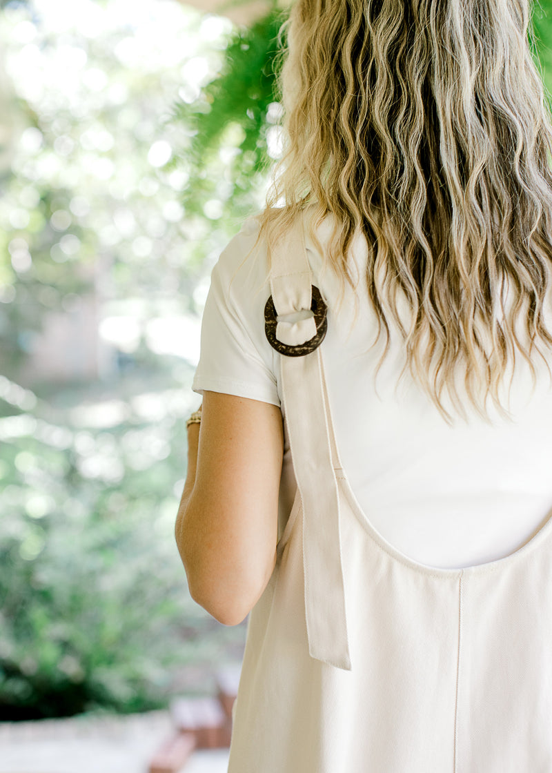 Close up of faux wood adjustable straps on the back of a cream jumpsuit. 