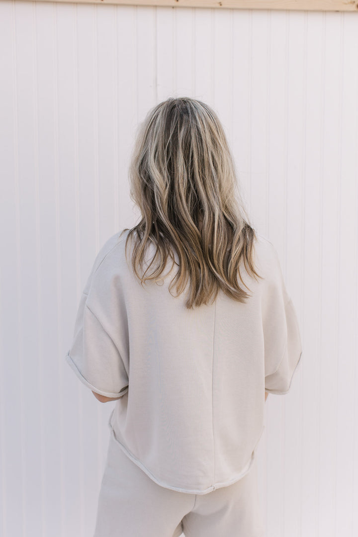 Back view of Model wearing a cream short sleeve sweatshirt with a rolled hem and pouch pocket.