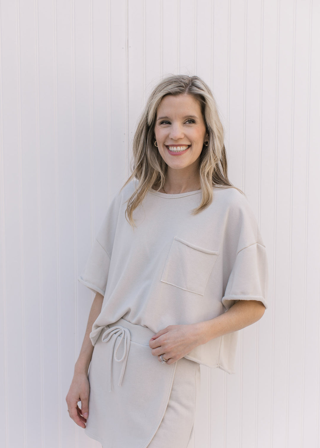 Model wearing a cream short sleeve sweatshirt with a rolled hem and pouch pocket.