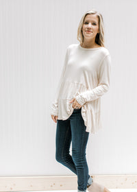 Model wearing jeans with a cream tiered top with long sleeves and composed of bamboo viscose. 