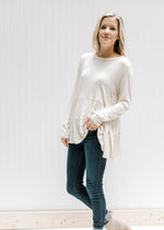 Model wearing jeans with a cream tiered top with long sleeves and composed of bamboo viscose. 