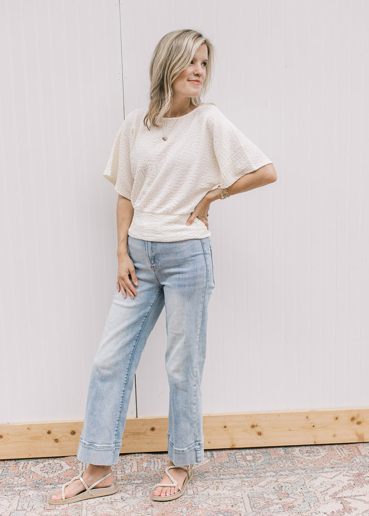 Model wearing a cream short sleeve top with round neck, elastic waist and slightly cropped.
