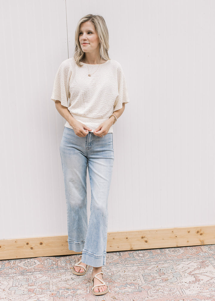 Model wearing a cream textured top with round neck, short sleeves and elastic waist. 
