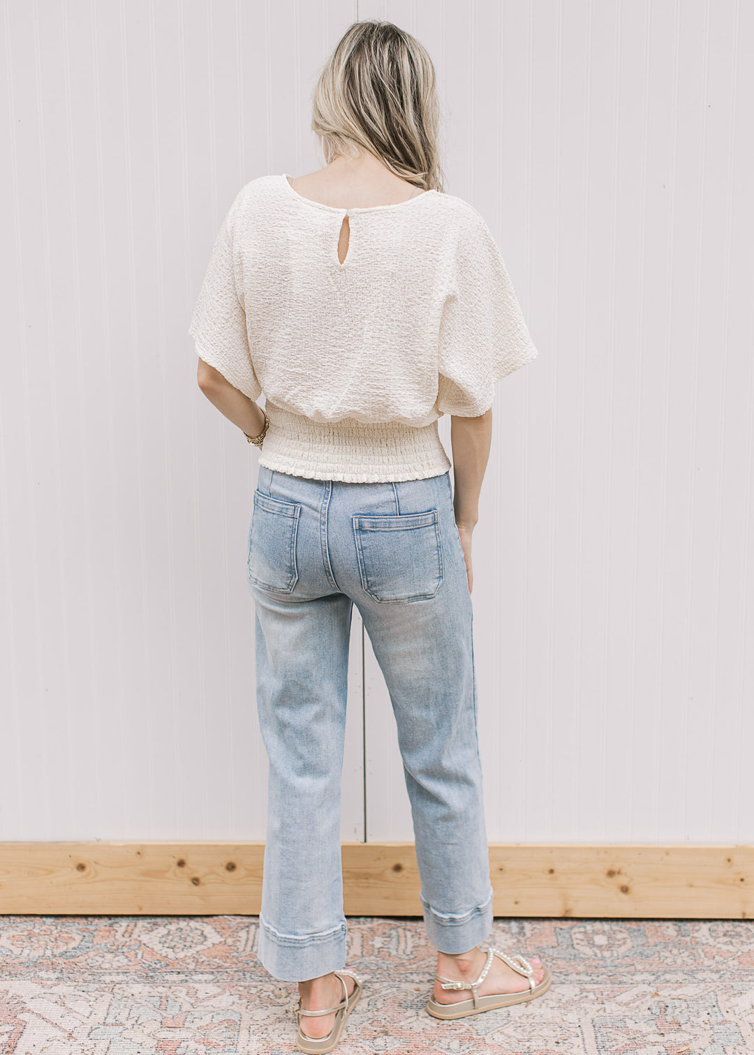 Back view of Model wearing a cream short sleeve top with keyhole, elastic waist and slightly crop.
