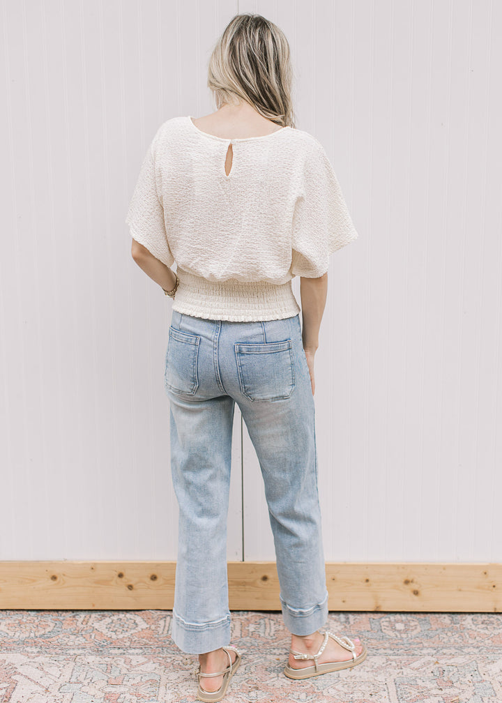 Back view of Model wearing a cream short sleeve top with keyhole, elastic waist and slightly crop.